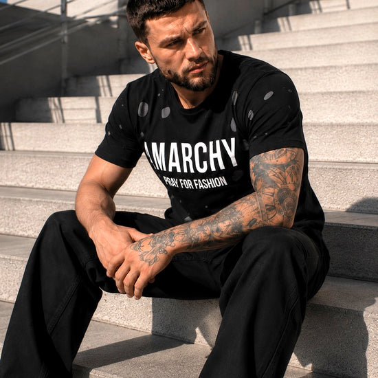 Чоловік у чорній двошаровій футболці ANARCHY KRUTYAKOV сидить на сходах