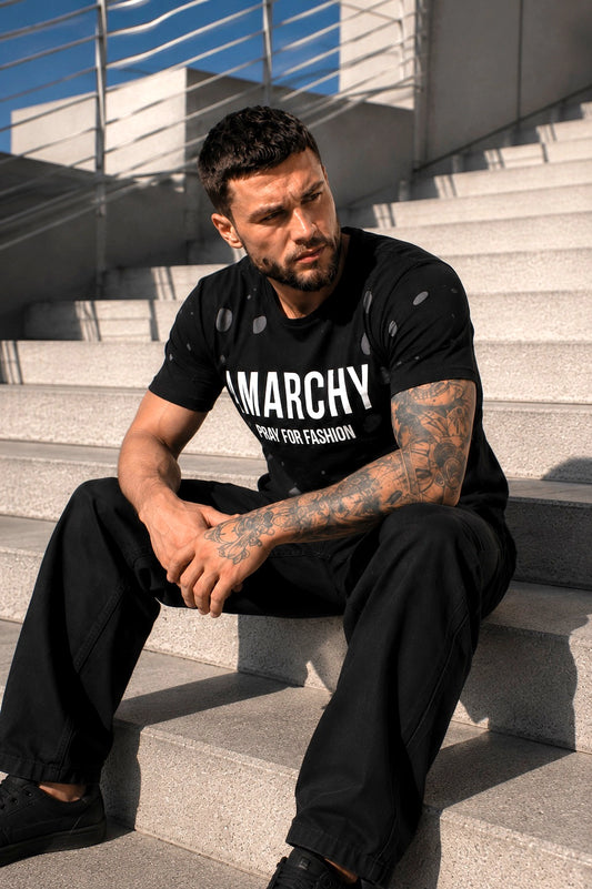 Чоловік у чорній двошаровій футболці ANARCHY KRUTYAKOV сидить на сходах